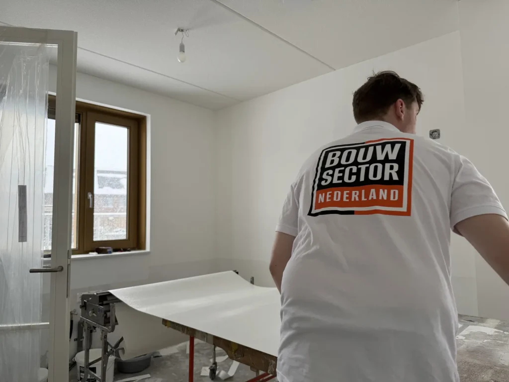 Behanger van Bouwsector Nederland met een baan behang op de plaktafel in een nieuwbouwkamer