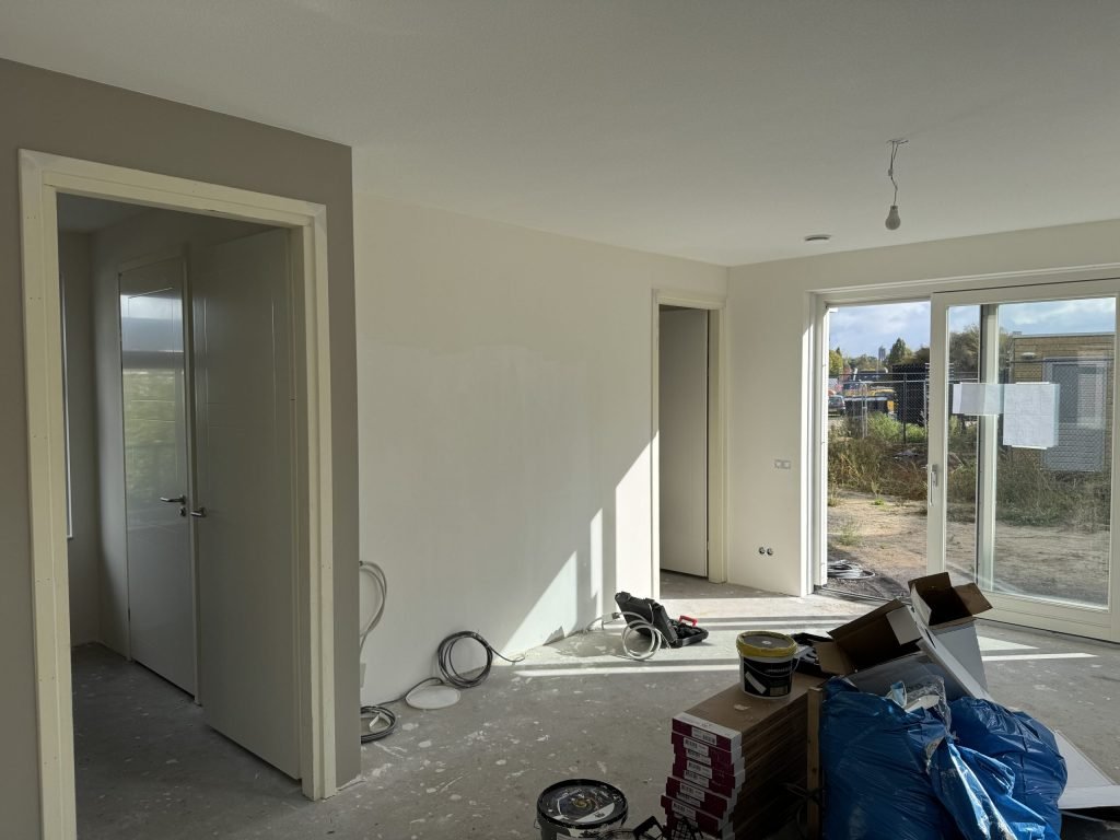 Pas opgeleverde nieuwbouwwoning met kale wanden, openstaande binnendeuren en een tuindeur naar een bouwterrein