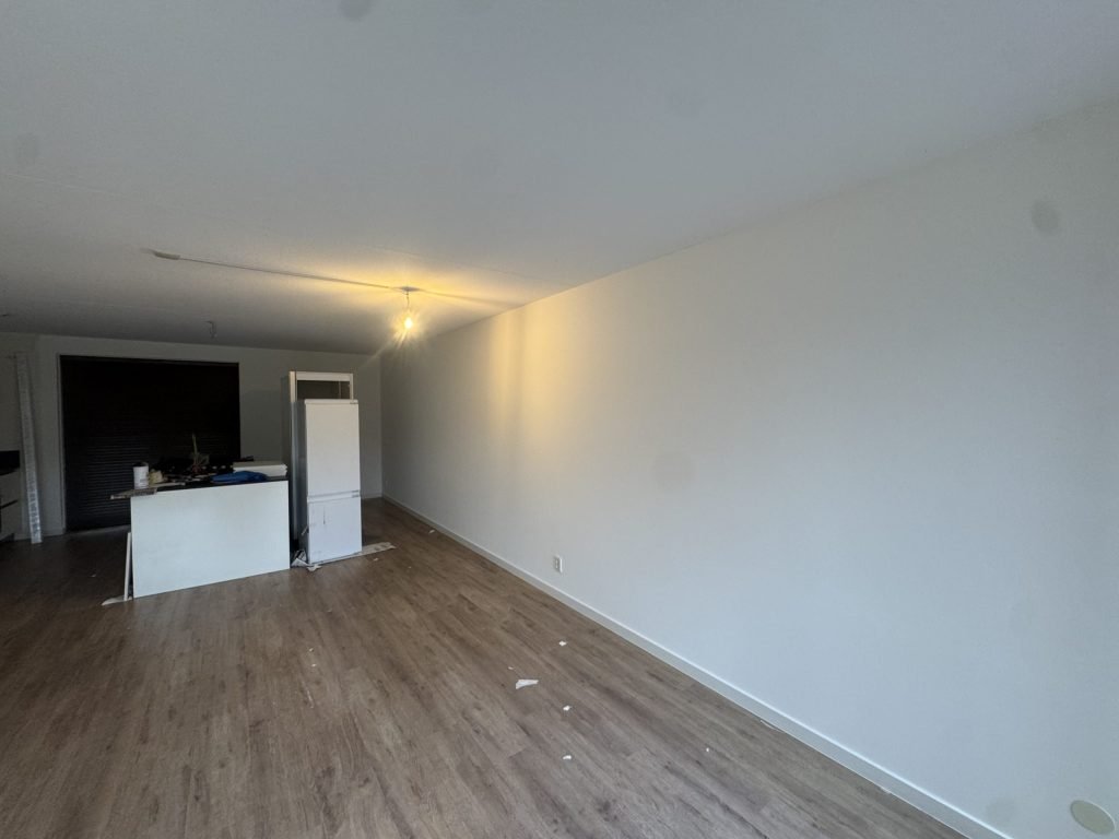 Lange lichte wand in de woonkamer van een appartement met houten vloer en open keuken